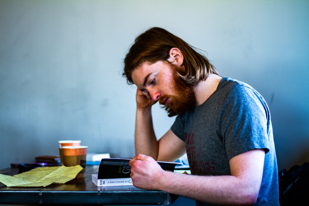 A homeowner sits at their kitchen table with a frustrated expression, looking over complex insurance claim forms related to property damage.