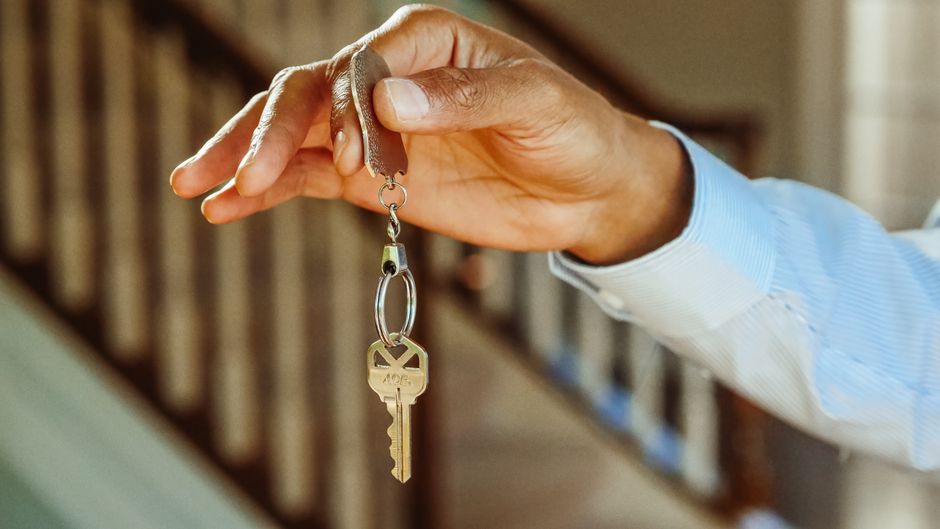 A person's hand holding a set of modern house keys, representing the tangible investment and ownership opportunity of a low-cost real estate franchise.