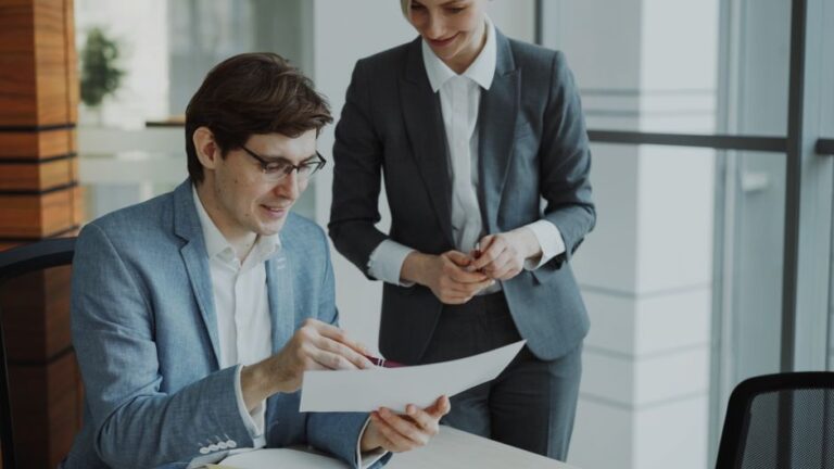 Two savvy real estate professionals collaborating over architectural blueprints in a bright, modern office, symbolizing st...